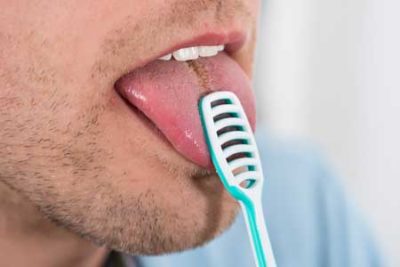 man scraping his tongue to prevent bad breath